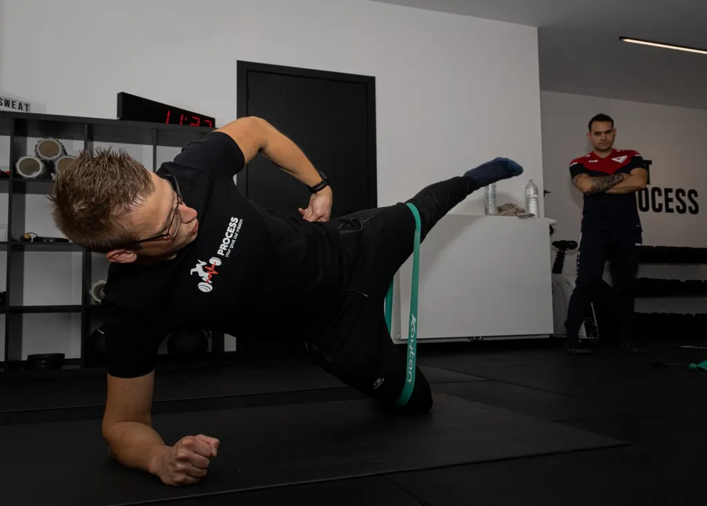 Een sporter voert een side plank uit met een weerstandsband, begeleid door een Process-coach in Balen