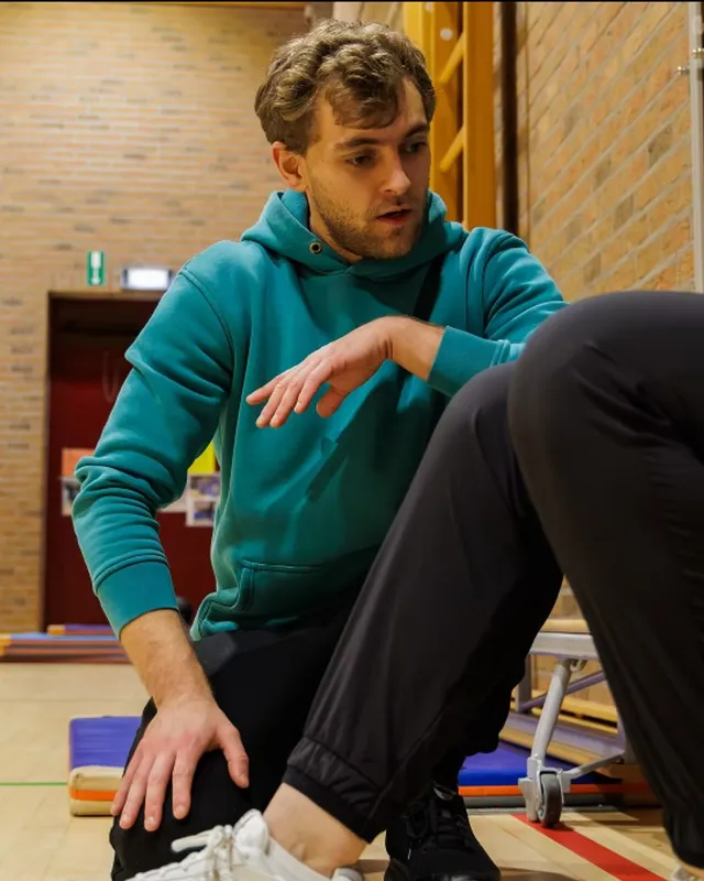 Mathijs Claes, coach bij Process, begeleidt een sporter tijdens een oefening op de mat